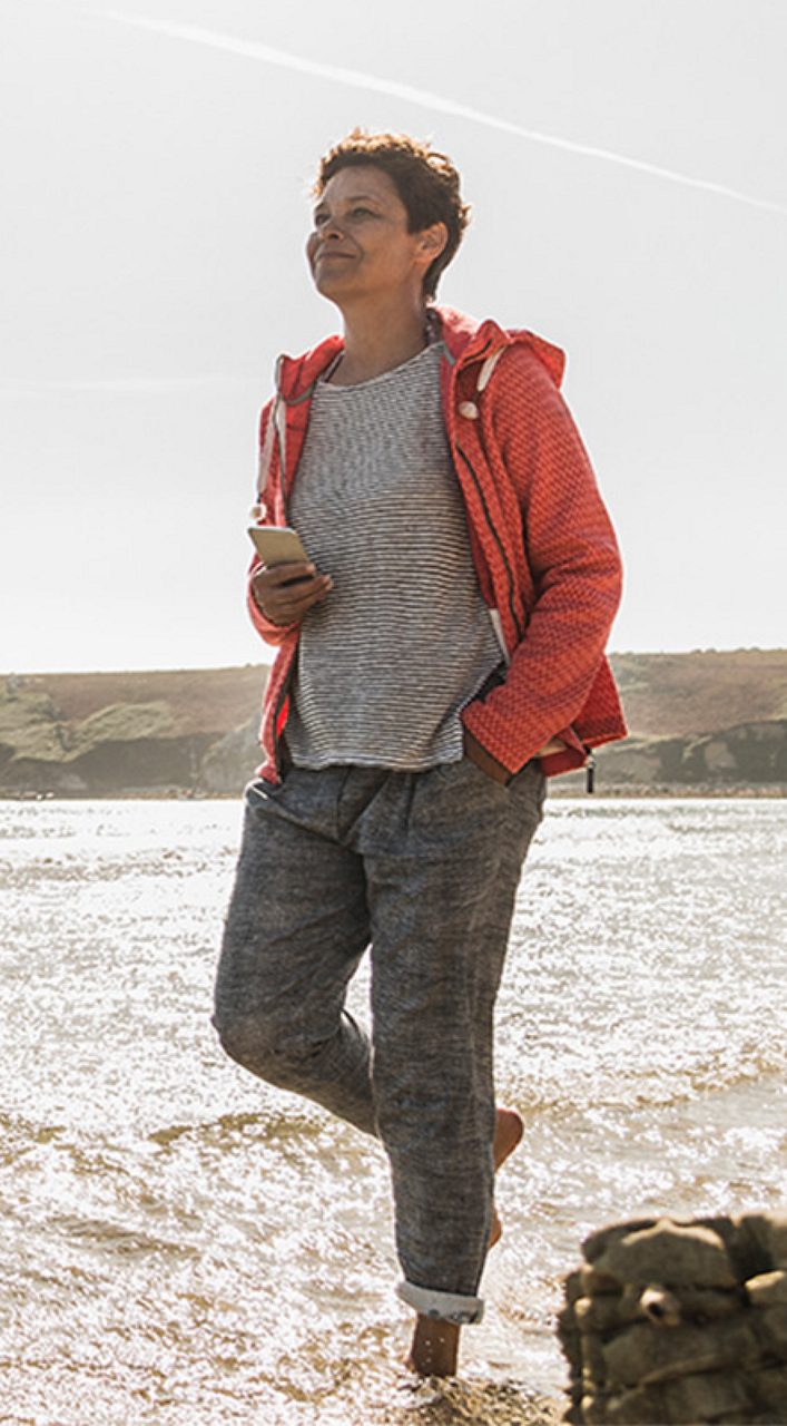 Image of a woman walking on the beach. She is wearing a red jacket