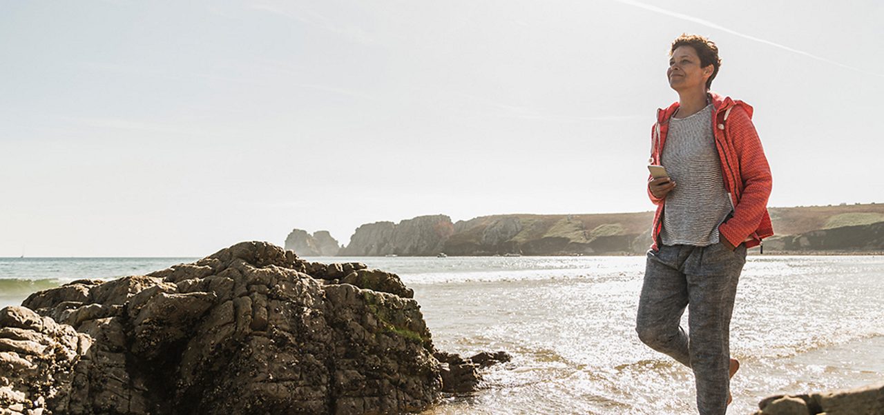 Image of a woman walking on the beach. She is wearing a red jacket