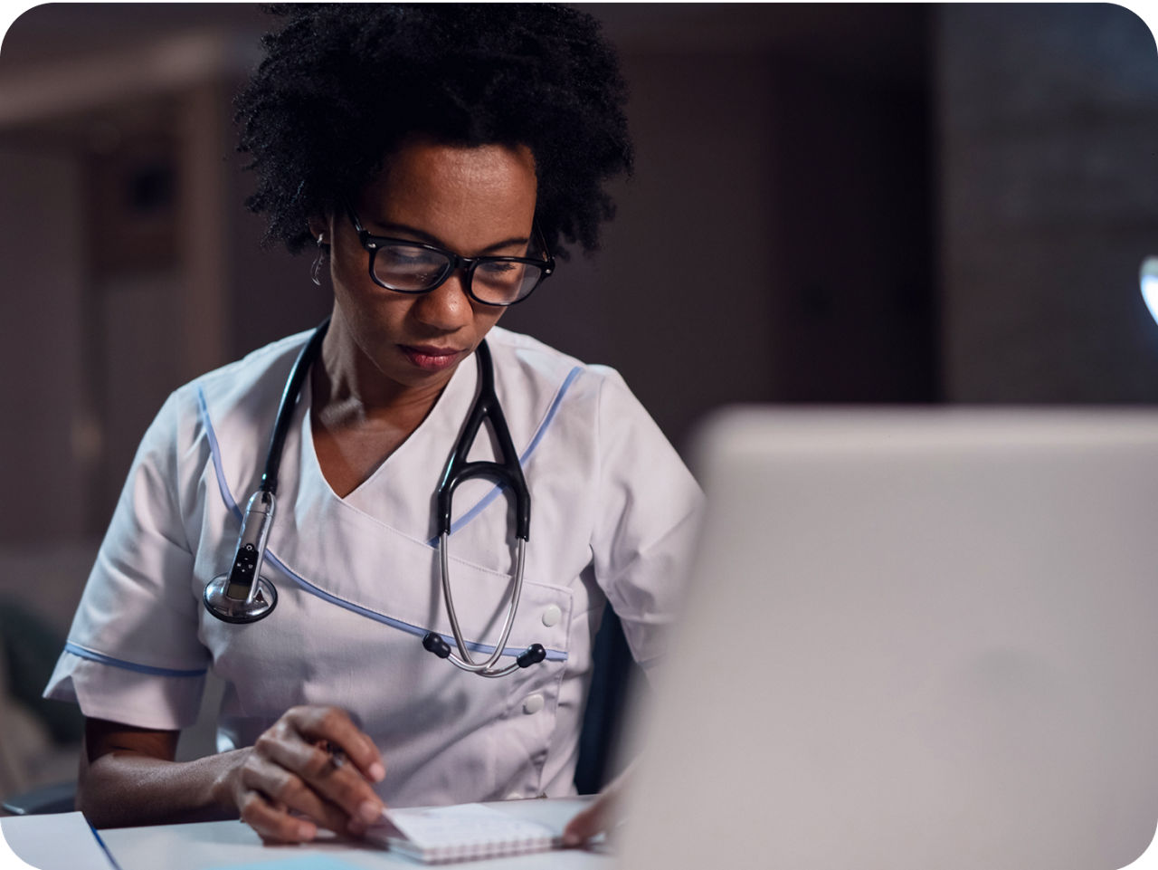 Image of a woman reading on a tablet. She is wearing glasses and a white scrub
