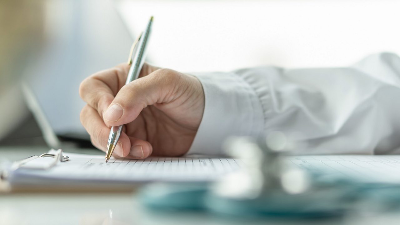 Medical doctor writing on patient personal health care record discharge form, or prescription paperwork in hospital office, clinic center for healthcare and life insurance concept