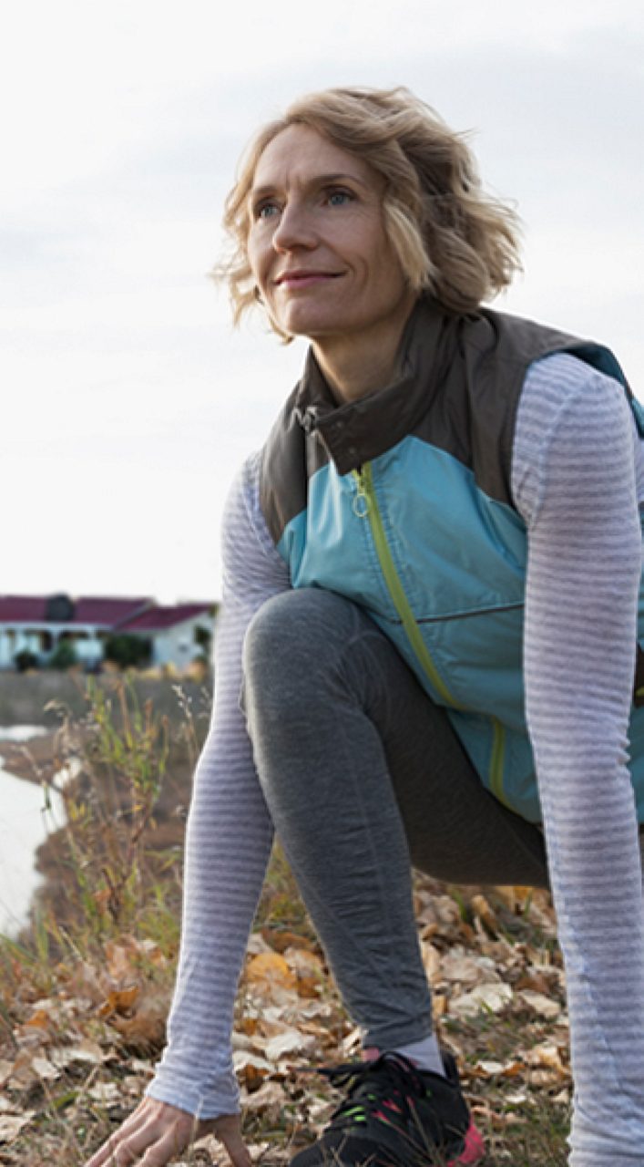 Image of a woman stretching. She is wearing a light blue vest.