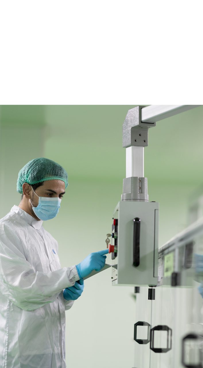 Astellas scientist wearing a white lab coat, medical mask, and rubber gloves, working with lab equipment in a high-tech research facility.