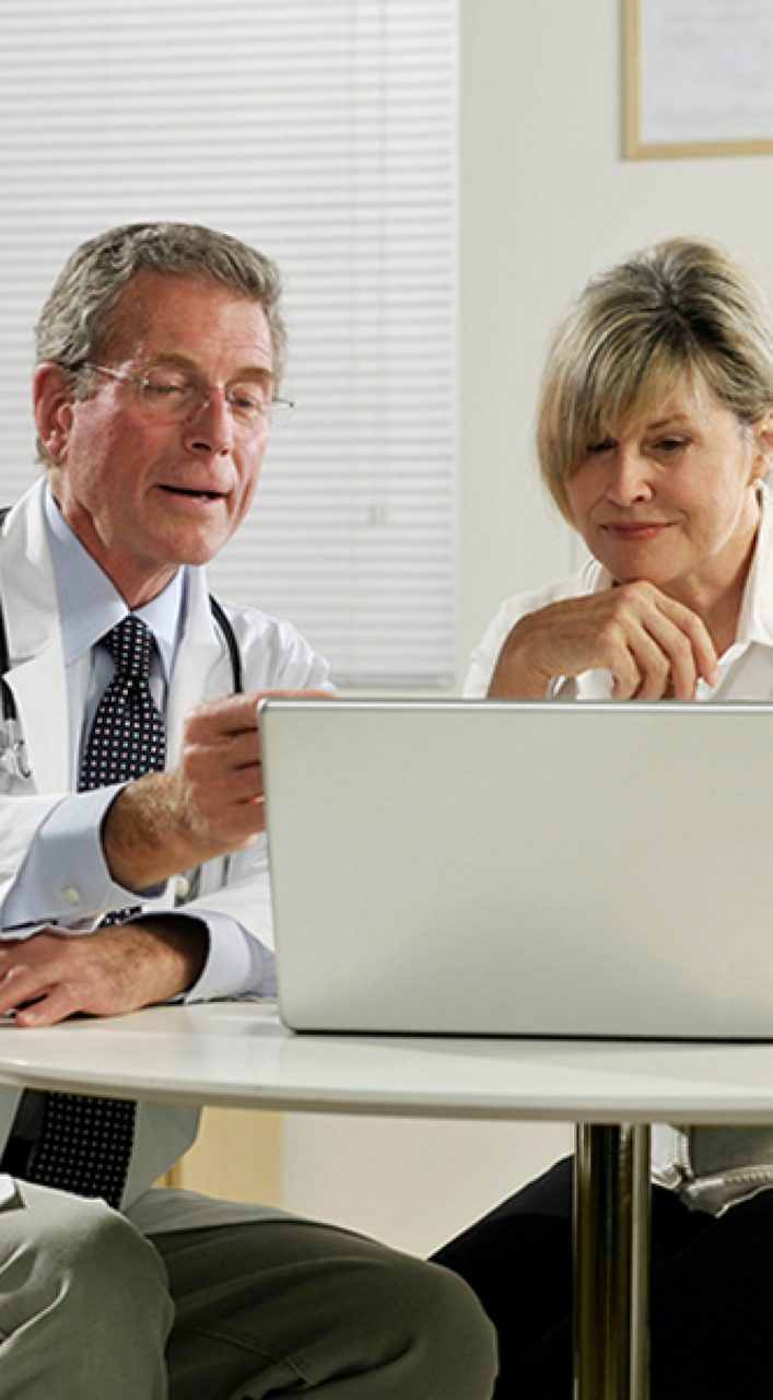 Image of a woman talking with a healthcare professional walking on the beach. She is wearing a red jacket